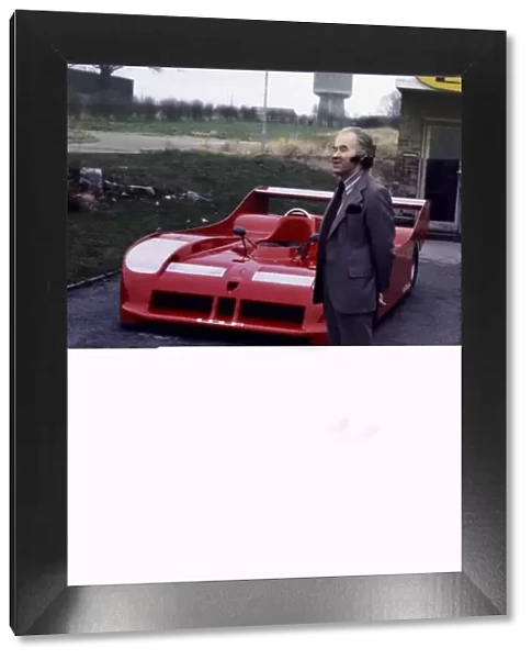 Eric Broadley stands in front of a Lola sportscar, portrait