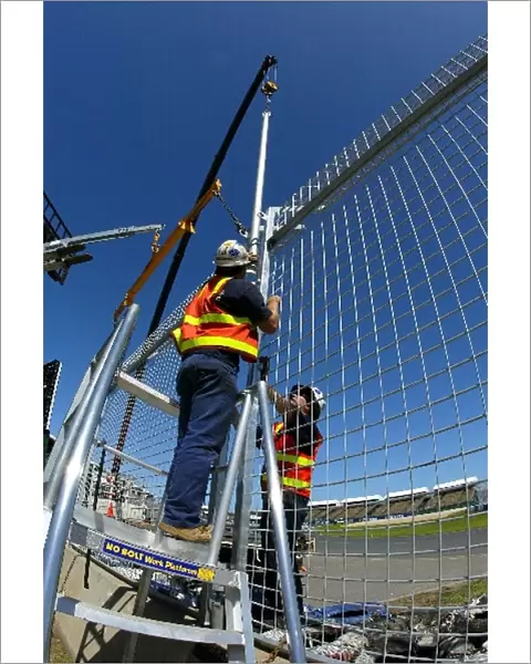 Formula One World Championship: Workmen construct the high catch fencing around the circuit