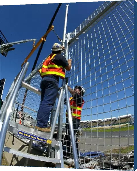 Formula One World Championship: Workmen construct the high catch fencing around the circuit