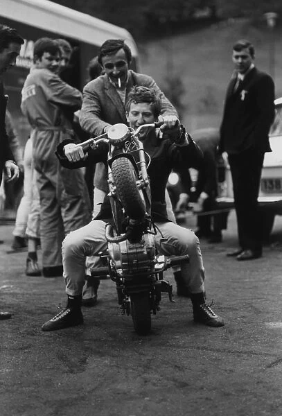 1965 Pau Grand Prix: Jochen Rindt, 1st position, on a moped with Charlie Crighton-Stuart and Jackie Stewart looking on, portrait
