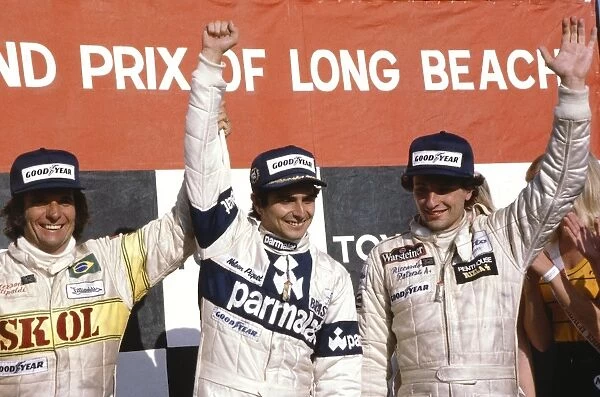 1980 United States Grand Prix West: Nelson Piquet celebrates 1st position on the podium with Riccardo Patrese 2nd position and Emerson Fittipaldi