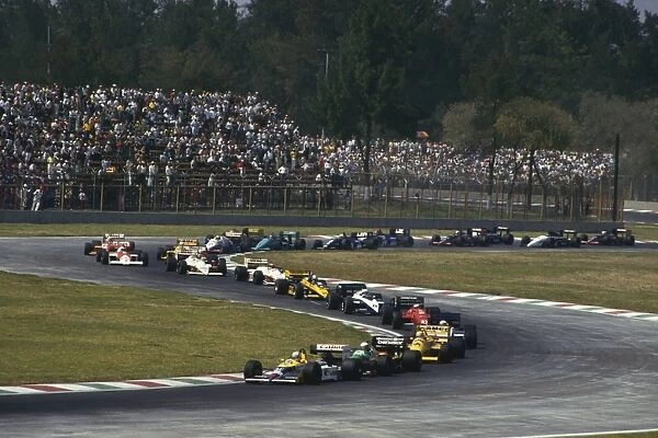 1987 Mexican Grand Prix: Nigel Mansell 1st position, leads Teo Fabi, Ayrton Senna and the rest of the field on the first lap