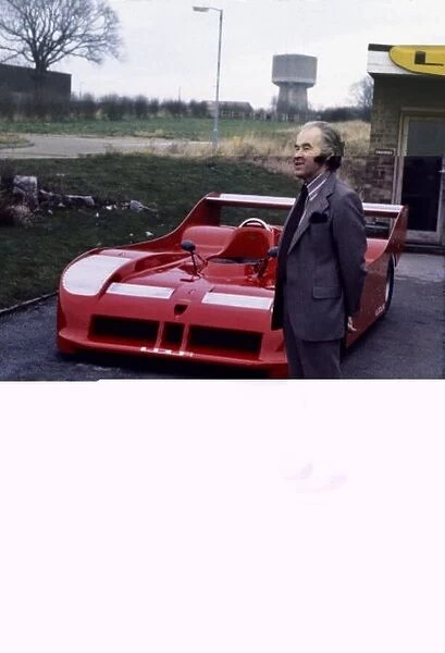 Eric Broadley stands in front of a Lola sportscar, portrait