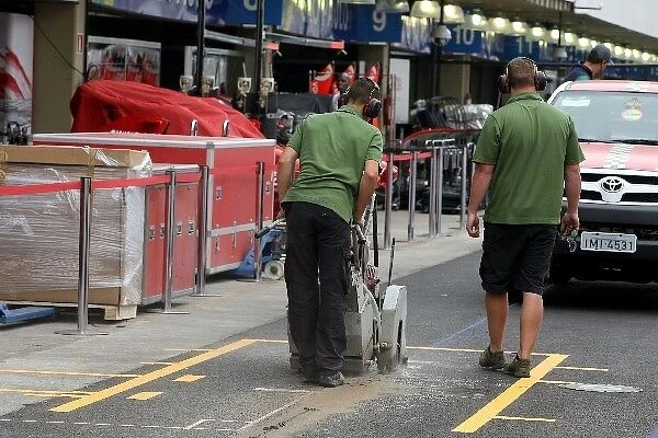 Formula One World Championship: A man cuts the surface of the pitlane with a machine