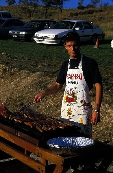 Formula One World Championship: Mark Webber Minardi, tries his hand at cooking sausages on a Barbie"