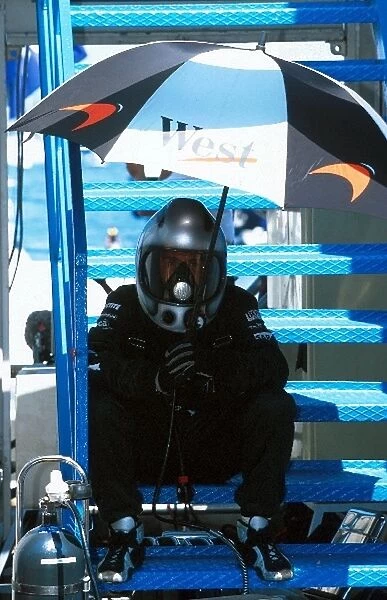 Formula One World Championship: A McLaren mechanic seeks shelter from the sun in a cramped pit lane