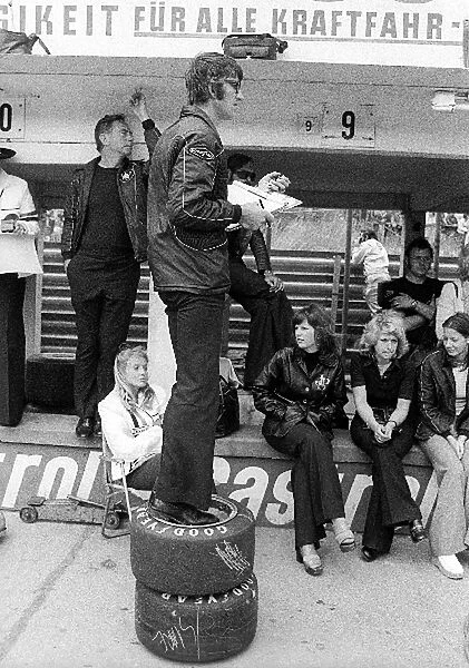 Formula One World Championship: Peter Warr Lotus Team Manager uses a stack of tyres to get a better vantage point in the pits whilst timing the