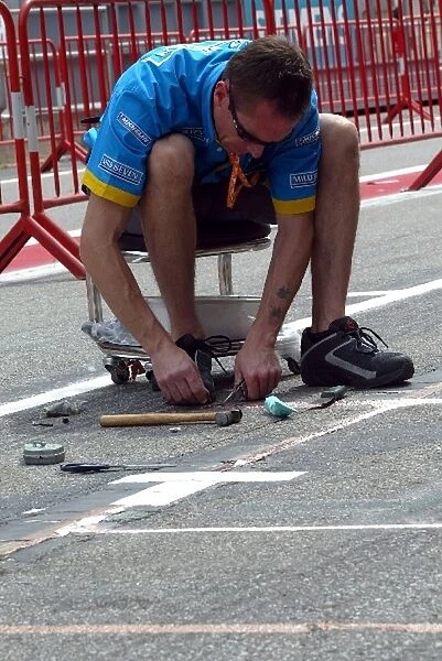 Formula One World Championship: A Renault mechanic sets up the pit box markings in the pit lane