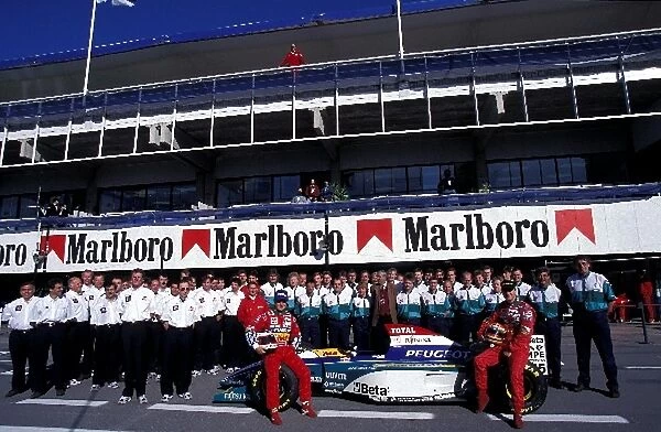 Formula One World Championship: Rubens Barrichello Jordan and Eddie Irvine Jordan pose with the rest of the Jordan Team and Peugeot Engineers