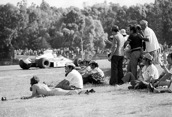 Formula One World Championship: Spectators watch race winner Denny Hulme McLaren M23 by the side of the circuit