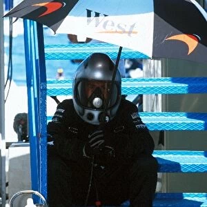 Formula One World Championship: A McLaren mechanic seeks shelter from the sun in a cramped pit lane