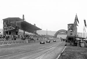 1961 French Grand Prix - Masten Gregory: Masten Gregory follows a group of cars passed the pits and main grandstand