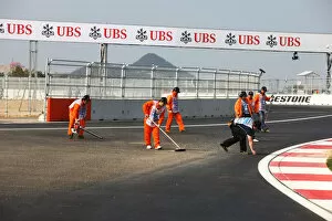 Formula One World Championship: Marshals clear dirt and stones from the final corner at the end of the session